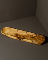 An olive wood bread slicing board with natural edges and grooves, placed on a dark background.